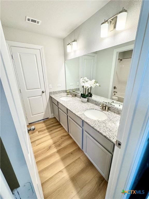 full bathroom featuring double vanity, visible vents, a sink, and wood finished floors