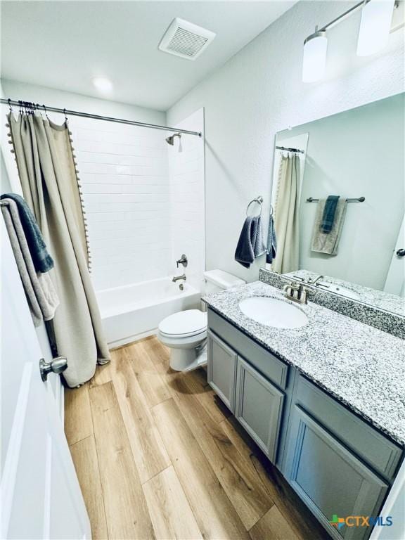 bathroom with visible vents, toilet, wood finished floors, shower / bath combo with shower curtain, and vanity