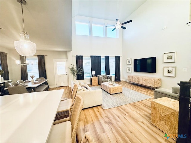 living area with baseboards, high vaulted ceiling, light wood-style flooring, and a ceiling fan