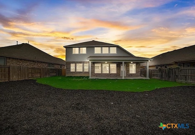 back of property at dusk featuring a patio, a lawn, and a fenced backyard