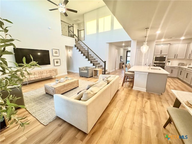 living room with a ceiling fan, baseboards, stairs, visible vents, and light wood-style floors