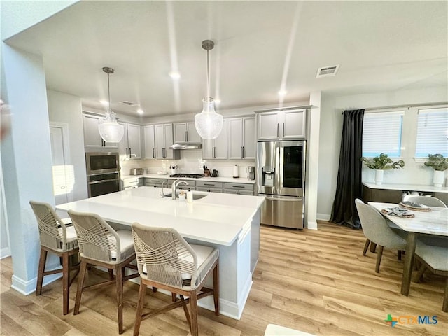 kitchen with appliances with stainless steel finishes, light countertops, a sink, and backsplash