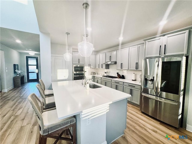 kitchen featuring under cabinet range hood, gas stovetop, light wood-type flooring, stainless steel refrigerator with ice dispenser, and tasteful backsplash