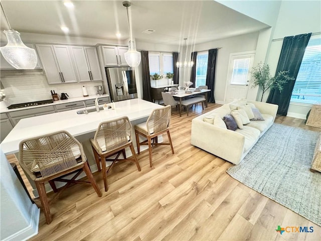 kitchen with stainless steel fridge with ice dispenser, black stovetop, light countertops, light wood-type flooring, and a sink