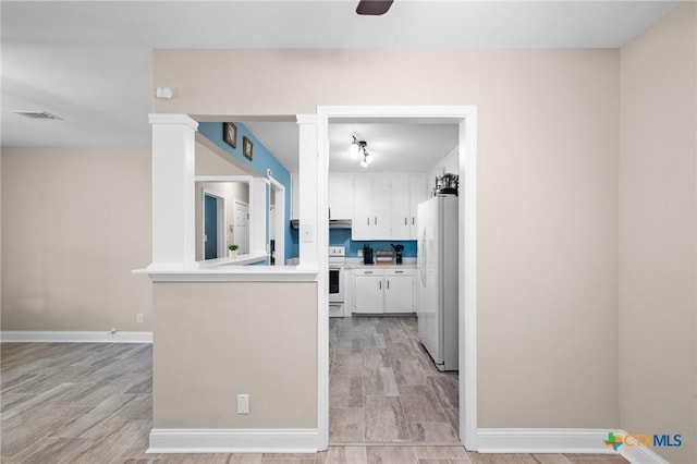 kitchen with white cabinets, baseboards, freestanding refrigerator, visible vents, and stove