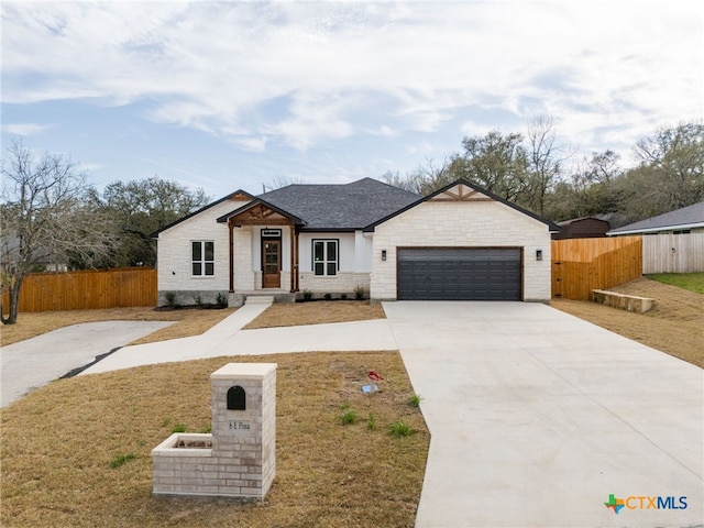 view of front facade with roof with shingles, fence, a garage, stone siding, and driveway