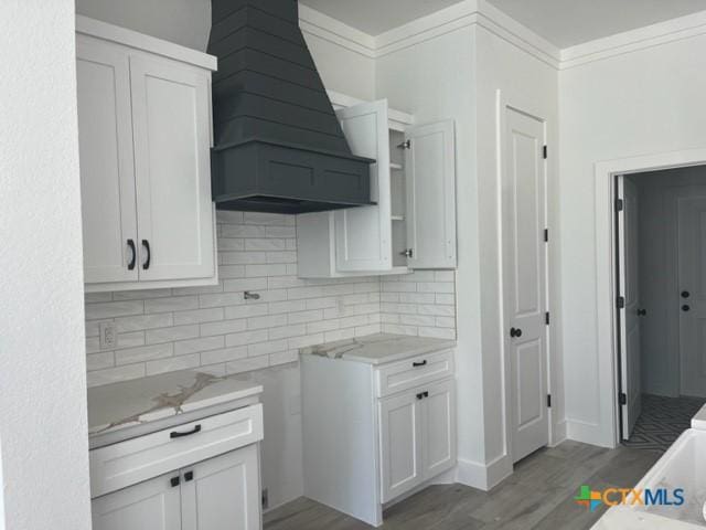 kitchen featuring white cabinetry, premium range hood, backsplash, and light wood-type flooring