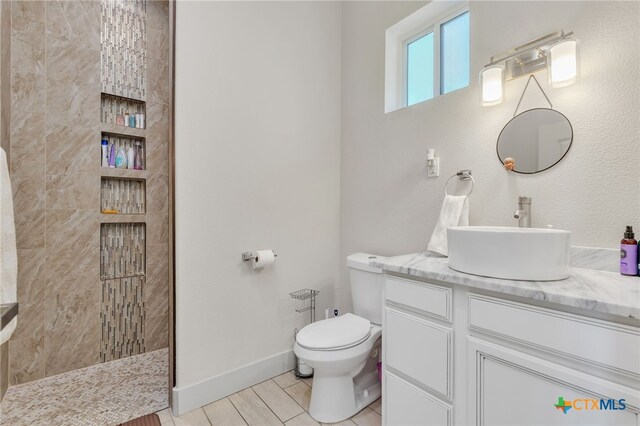 bathroom with a tile shower, vanity, and toilet