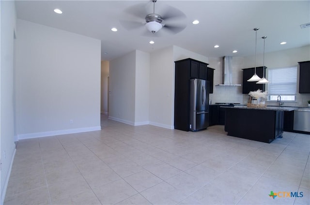 kitchen with ceiling fan, a sink, stainless steel appliances, wall chimney range hood, and backsplash