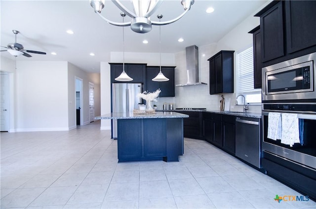 kitchen featuring a kitchen island, light stone countertops, appliances with stainless steel finishes, wall chimney exhaust hood, and a sink