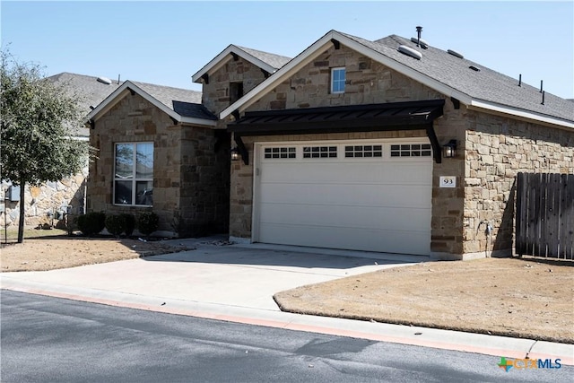 view of front of property with driveway, stone siding, fence, roof with shingles, and an attached garage