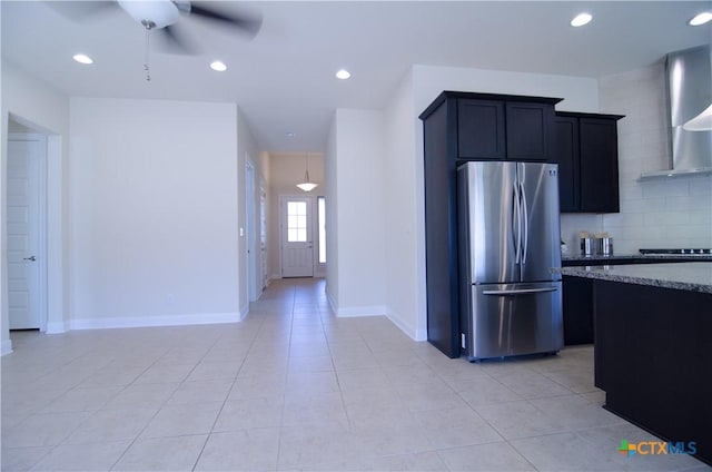 kitchen featuring tasteful backsplash, freestanding refrigerator, stone countertops, wall chimney exhaust hood, and a ceiling fan