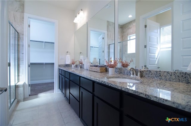 full bathroom with double vanity, a stall shower, a sink, tile patterned flooring, and a spacious closet