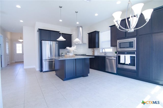 kitchen featuring light stone countertops, a kitchen island, stainless steel appliances, wall chimney range hood, and a chandelier