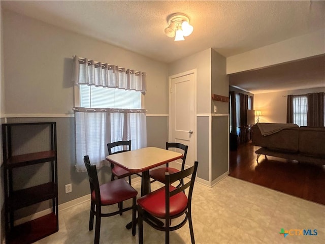 dining space with light floors, baseboards, and a textured ceiling