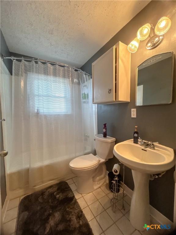 bathroom with a sink, tile patterned flooring, shower / tub combo, a textured ceiling, and toilet