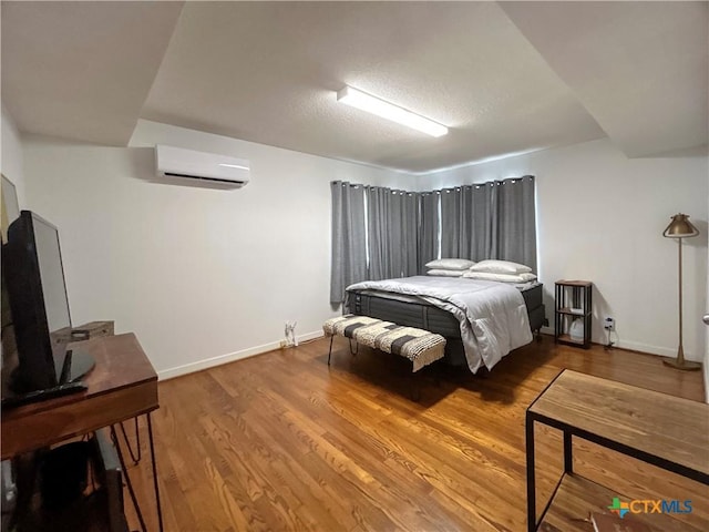 bedroom with baseboards, a textured ceiling, wood finished floors, and a wall unit AC