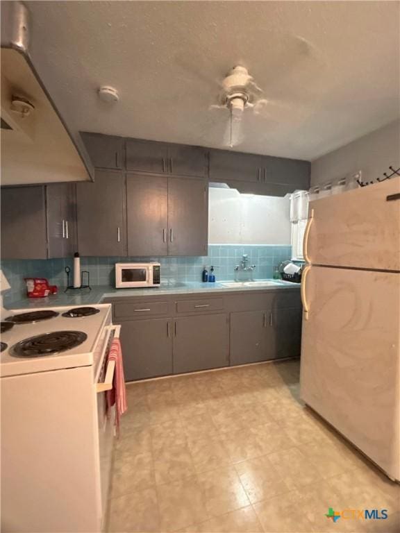 kitchen with gray cabinets, a sink, tasteful backsplash, white appliances, and light countertops