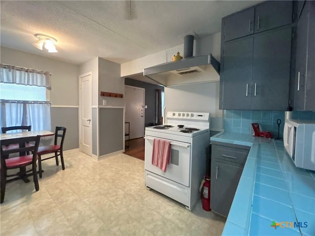 kitchen featuring a textured ceiling, tile countertops, white appliances, wall chimney exhaust hood, and light floors