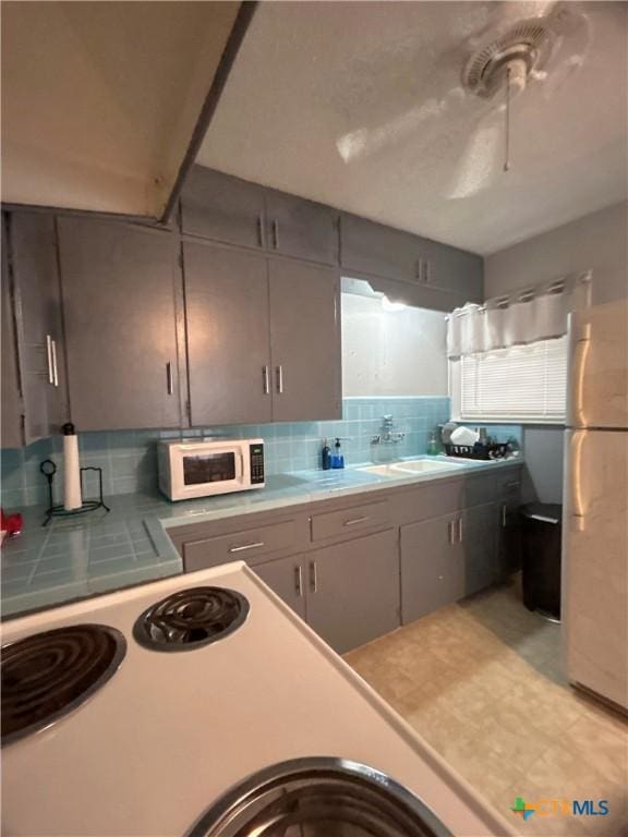 kitchen featuring decorative backsplash, white appliances, light countertops, and a sink