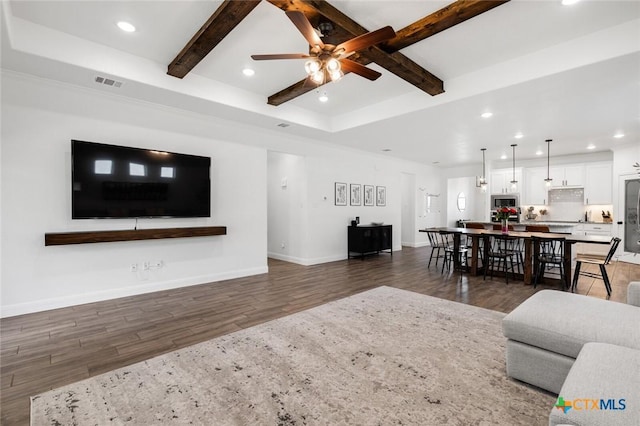 living room featuring dark hardwood / wood-style flooring, beam ceiling, a raised ceiling, and ceiling fan