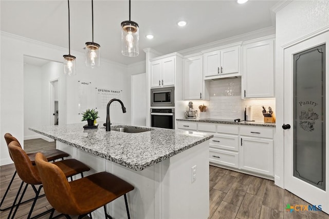 kitchen with appliances with stainless steel finishes, pendant lighting, sink, white cabinets, and a kitchen island with sink