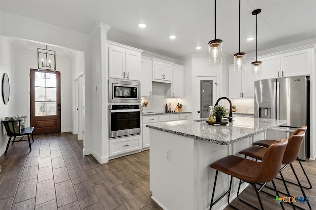 kitchen featuring appliances with stainless steel finishes, decorative light fixtures, an island with sink, and white cabinets