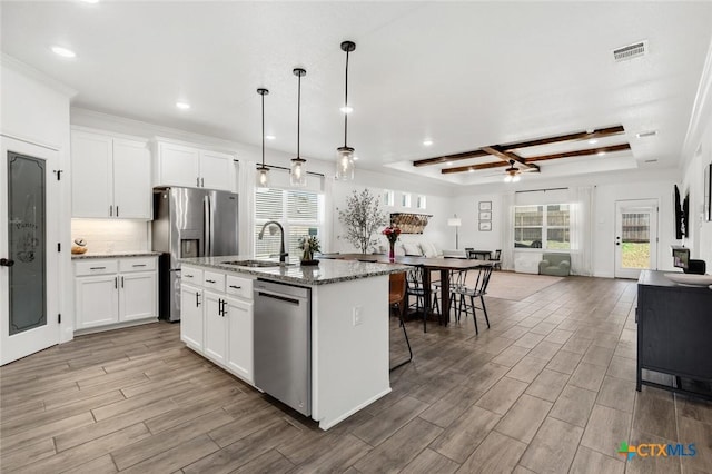 kitchen with light stone countertops, appliances with stainless steel finishes, a center island with sink, and white cabinets