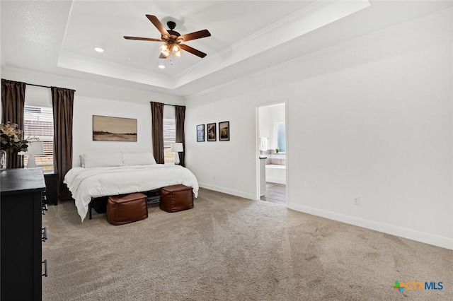 carpeted bedroom featuring crown molding, a tray ceiling, ensuite bath, and ceiling fan