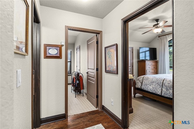 hallway with a textured wall, vaulted ceiling, baseboards, a textured ceiling, and dark wood finished floors