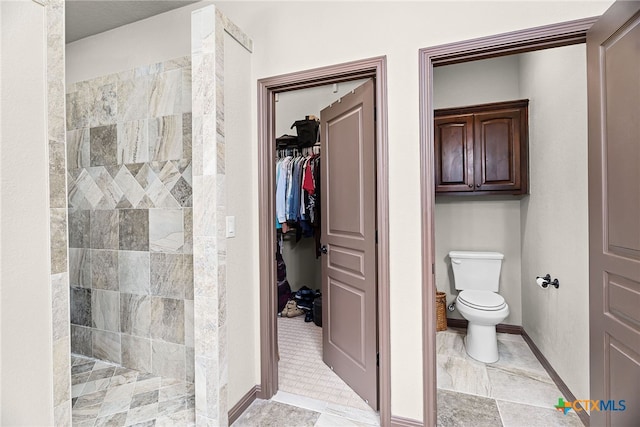 bathroom featuring toilet, a walk in closet, tiled shower, and baseboards