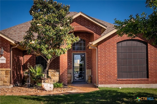 doorway to property featuring a shingled roof, an attached garage, and brick siding