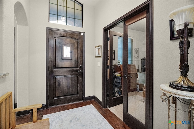 foyer featuring arched walkways, baseboards, and dark wood-type flooring
