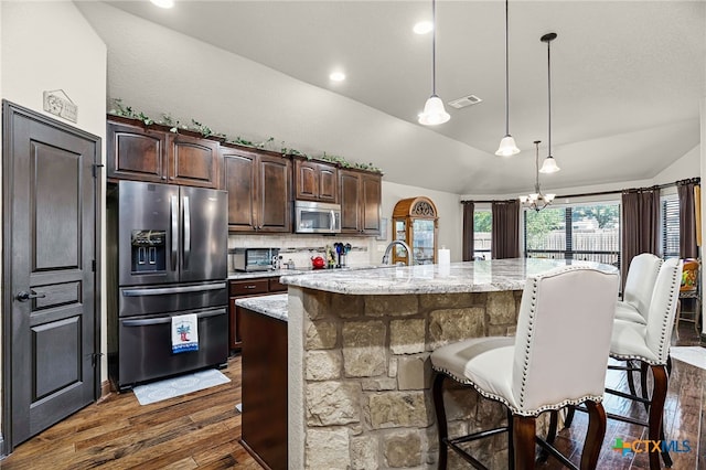 kitchen featuring appliances with stainless steel finishes, a breakfast bar, dark brown cabinets, vaulted ceiling, and dark wood finished floors
