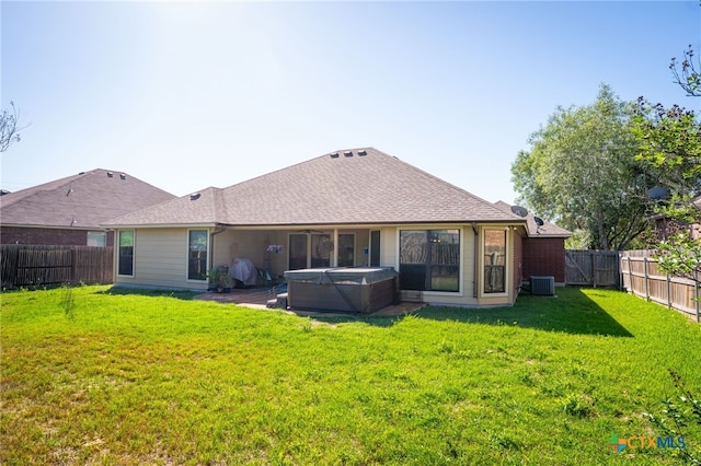 rear view of property featuring a hot tub, roof with shingles, a lawn, central AC unit, and a fenced backyard