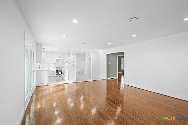 unfurnished living room featuring light wood-type flooring, visible vents, baseboards, and a sink