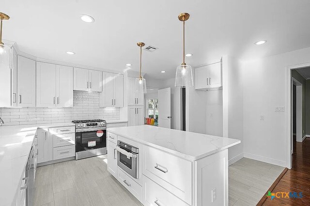 kitchen with visible vents, stainless steel gas range oven, white cabinetry, backsplash, and a center island