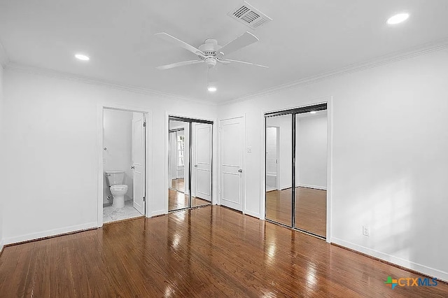 unfurnished bedroom with visible vents, two closets, baseboards, ornamental molding, and wood finished floors