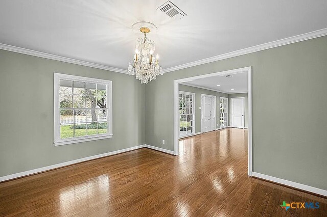 empty room with visible vents, baseboards, wood finished floors, and ornamental molding