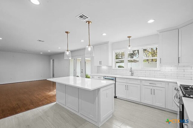 kitchen featuring backsplash, a kitchen island, stainless steel dishwasher, white cabinetry, and a sink