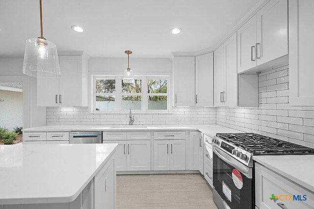 kitchen with white cabinets, pendant lighting, stainless steel gas range, and a sink