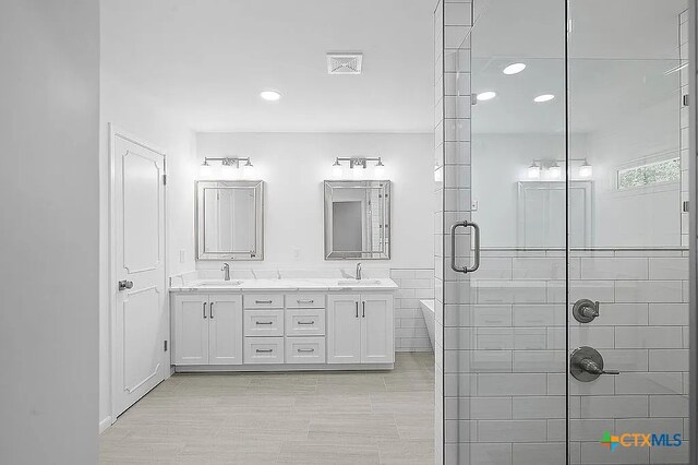 full bathroom with a sink, visible vents, tiled shower, and double vanity