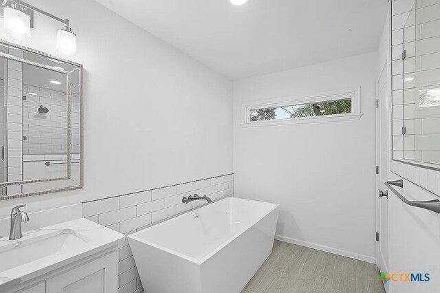 bathroom featuring tiled shower, a freestanding bath, tile walls, and vanity