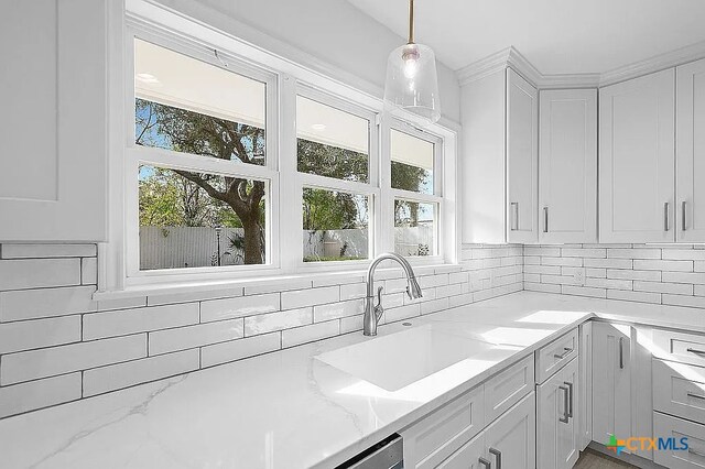 kitchen with a sink, decorative light fixtures, light stone counters, backsplash, and white cabinets