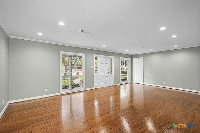 unfurnished living room with a healthy amount of sunlight, wood finished floors, and crown molding