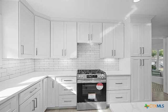 kitchen with stainless steel gas range oven, decorative backsplash, and white cabinetry