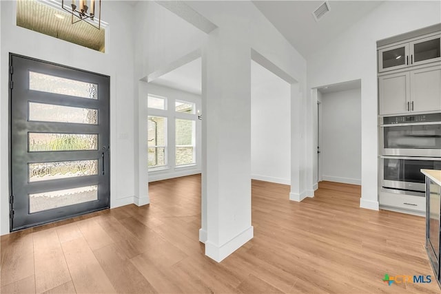 foyer with light hardwood / wood-style floors, high vaulted ceiling, and an inviting chandelier