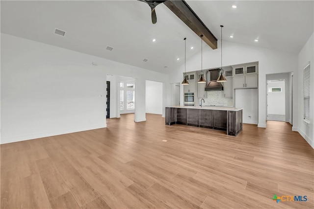 unfurnished living room featuring beam ceiling, light wood-type flooring, ceiling fan, and sink