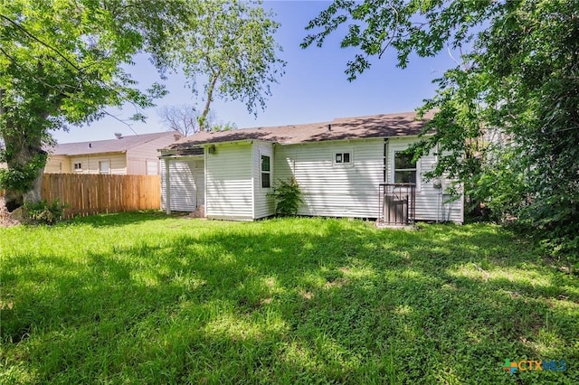 back of property with a lawn and fence