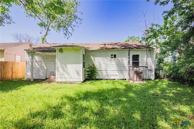 back of house with a lawn, fence, and roof with shingles